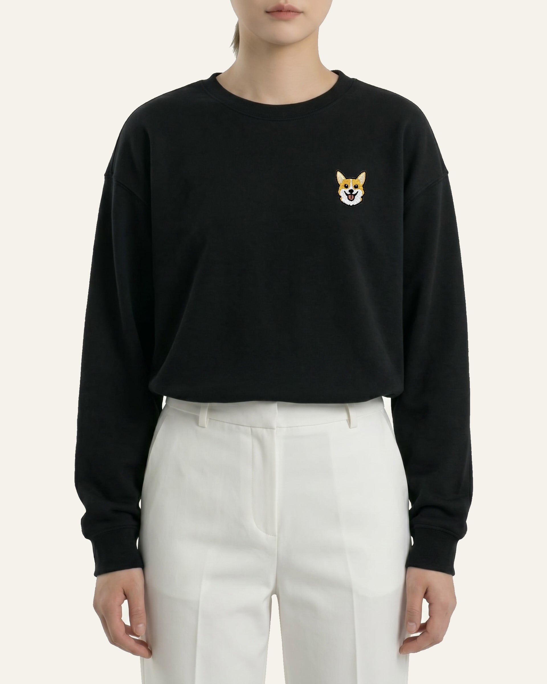 Woman wearing Black Sweatshirt with minimalist embroidered Corgi icon on left chest.