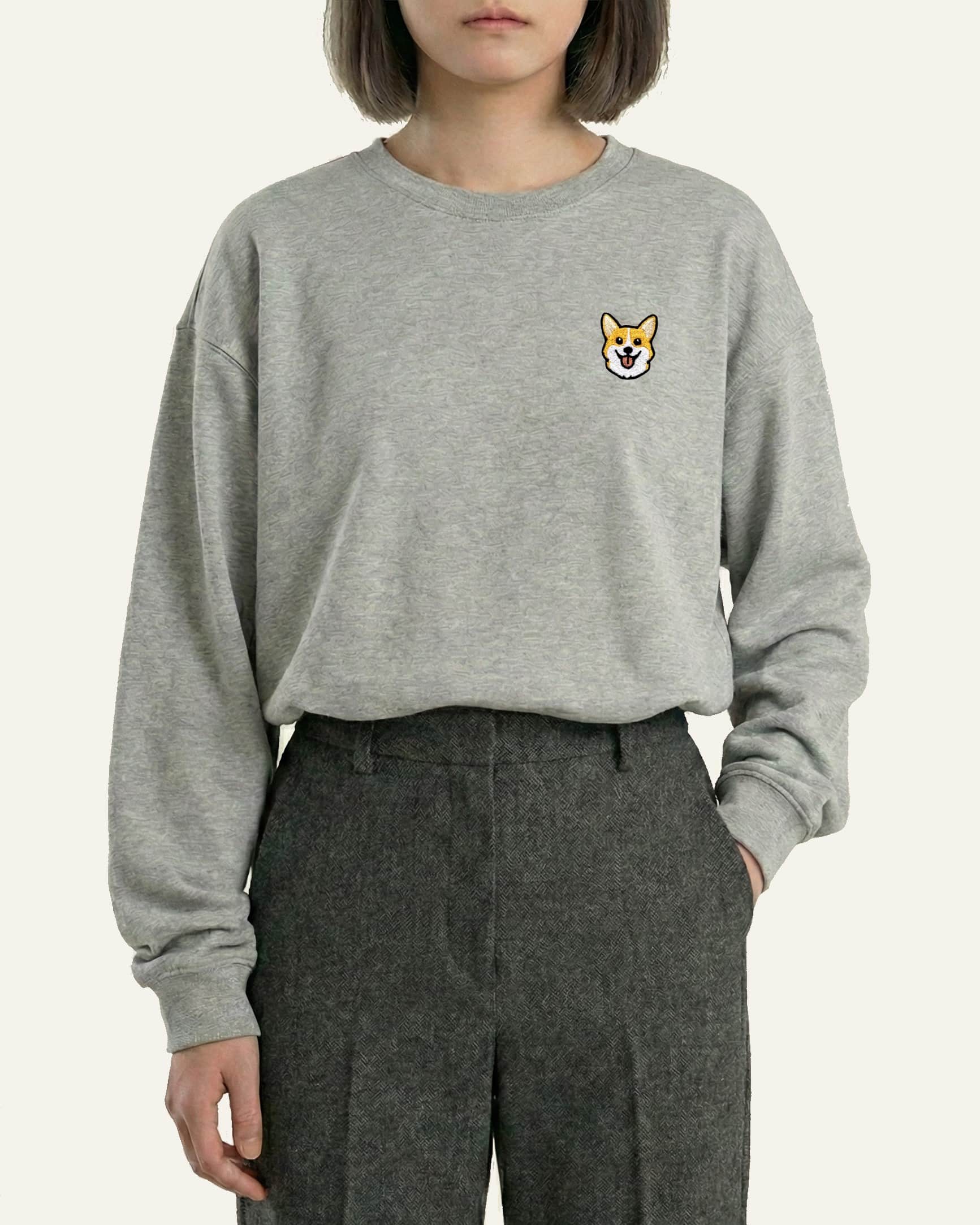 Woman wearing Light Grey Heather Sweatshirt with minimalist embroidered Corgi icon on left chest.