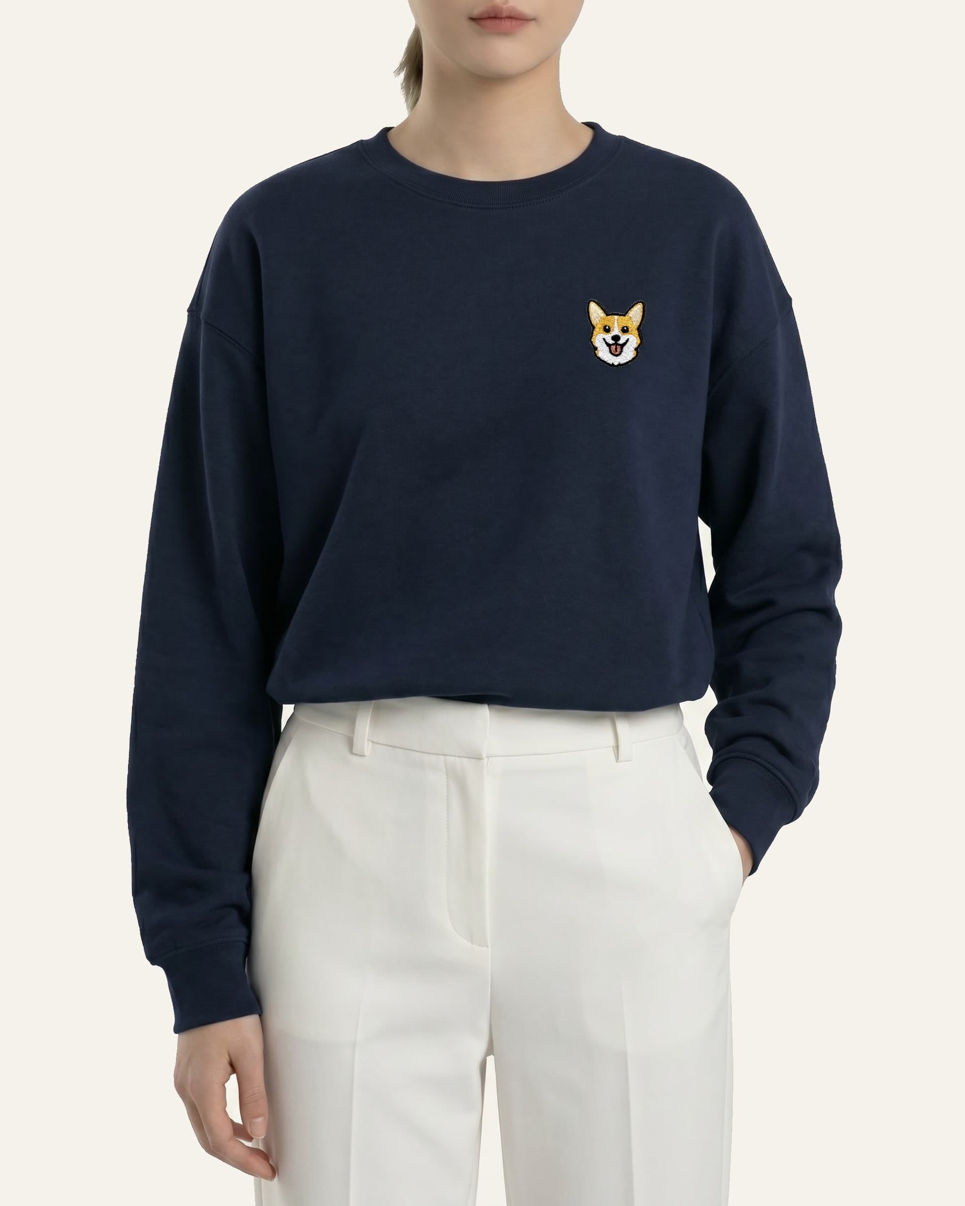 Woman wearing Navy Sweatshirt with minimalist embroidered Corgi icon on left chest.