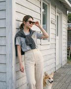 Woman standing outside wooden house wearing Light Grey Heather T-shirt with minimalist embroidered Corgi icon on left chest.