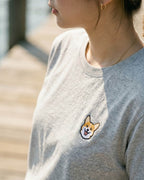 Close up of woman wearing Light Grey Heather T-shirt with minimalist embroidered Corgi icon on left chest.