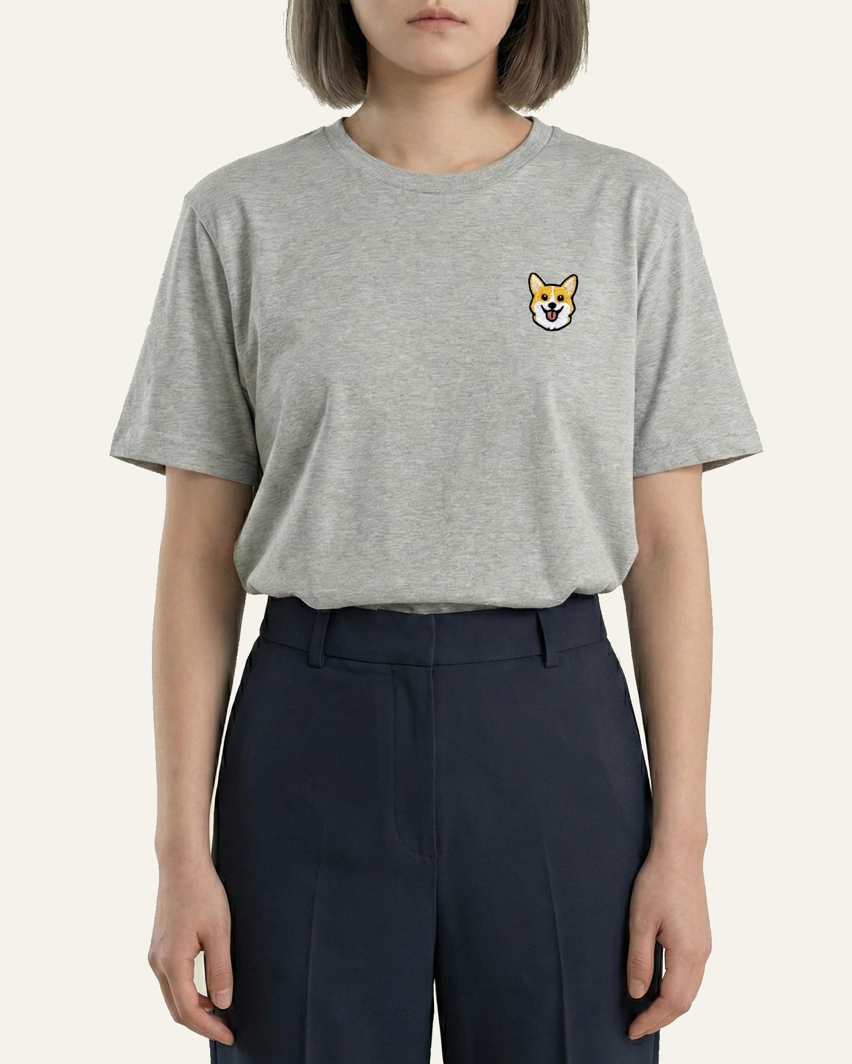 Woman wearing Light Grey Heather T-shirt with minimalist embroidered Corgi icon on left chest.