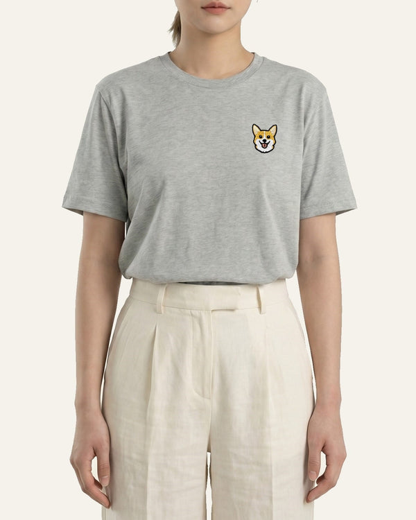 Woman wearing Light Grey Heather T-shirt with minimalist embroidered Corgi icon on left chest.