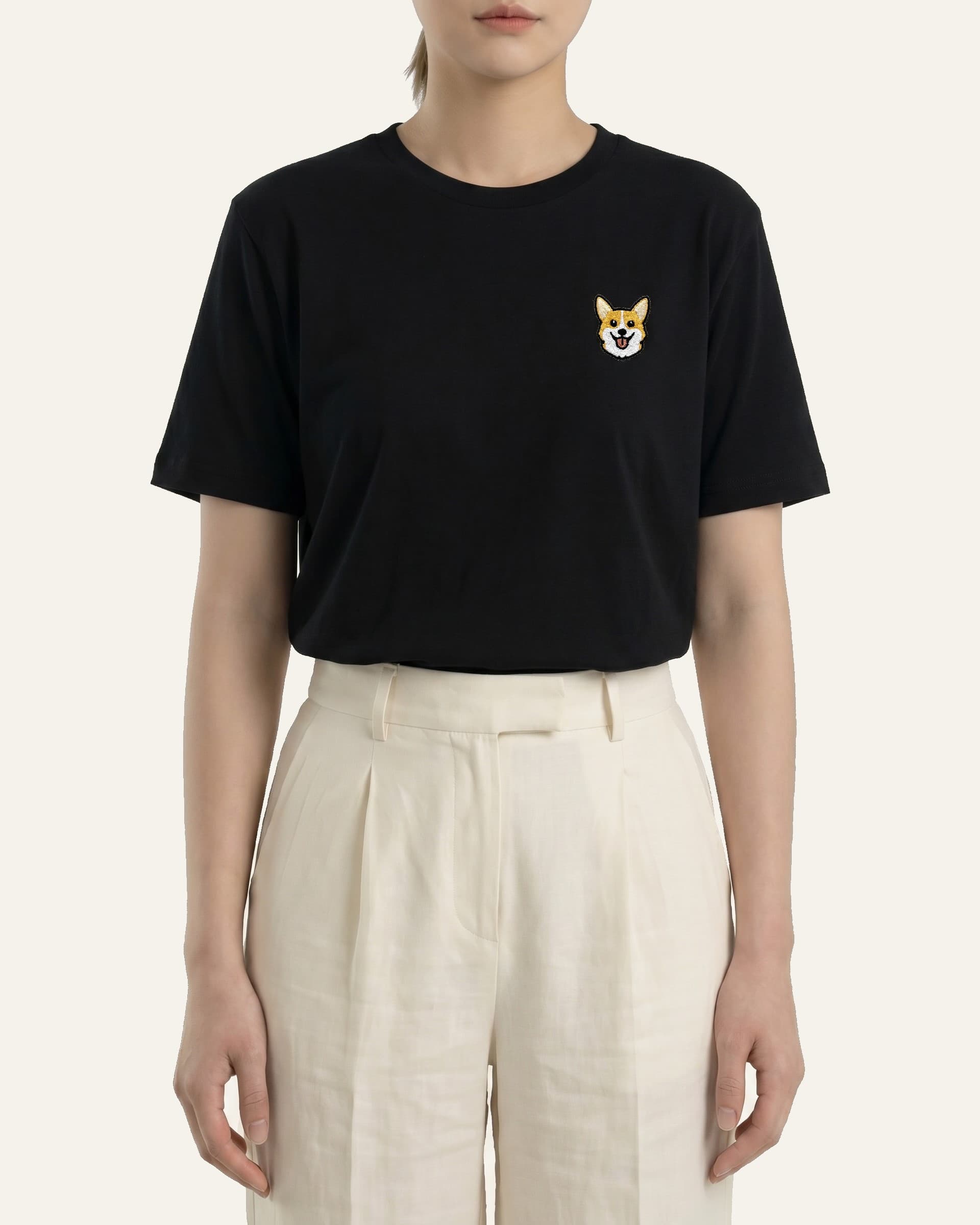 Woman wearing Black T-shirt with minimalist embroidered Corgi icon on left chest.
