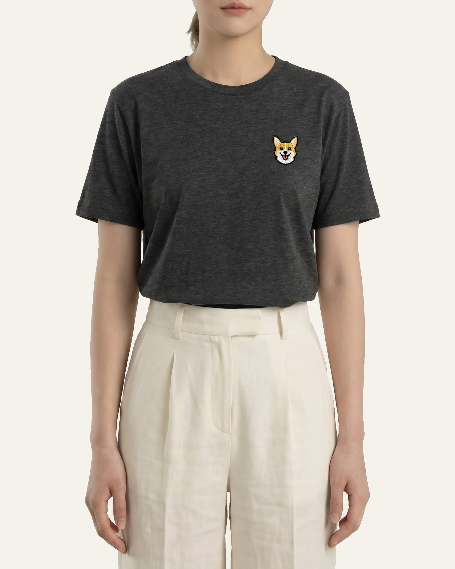 Woman wearing Dark Grey Heather T-shirt with minimalist embroidered Corgi icon on left chest.