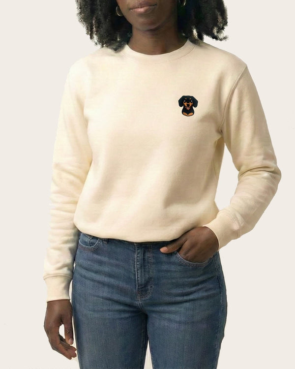 Woman wearing Light Beige Sweatshirt with minimalist embroidered Dachshund icon on left chest.