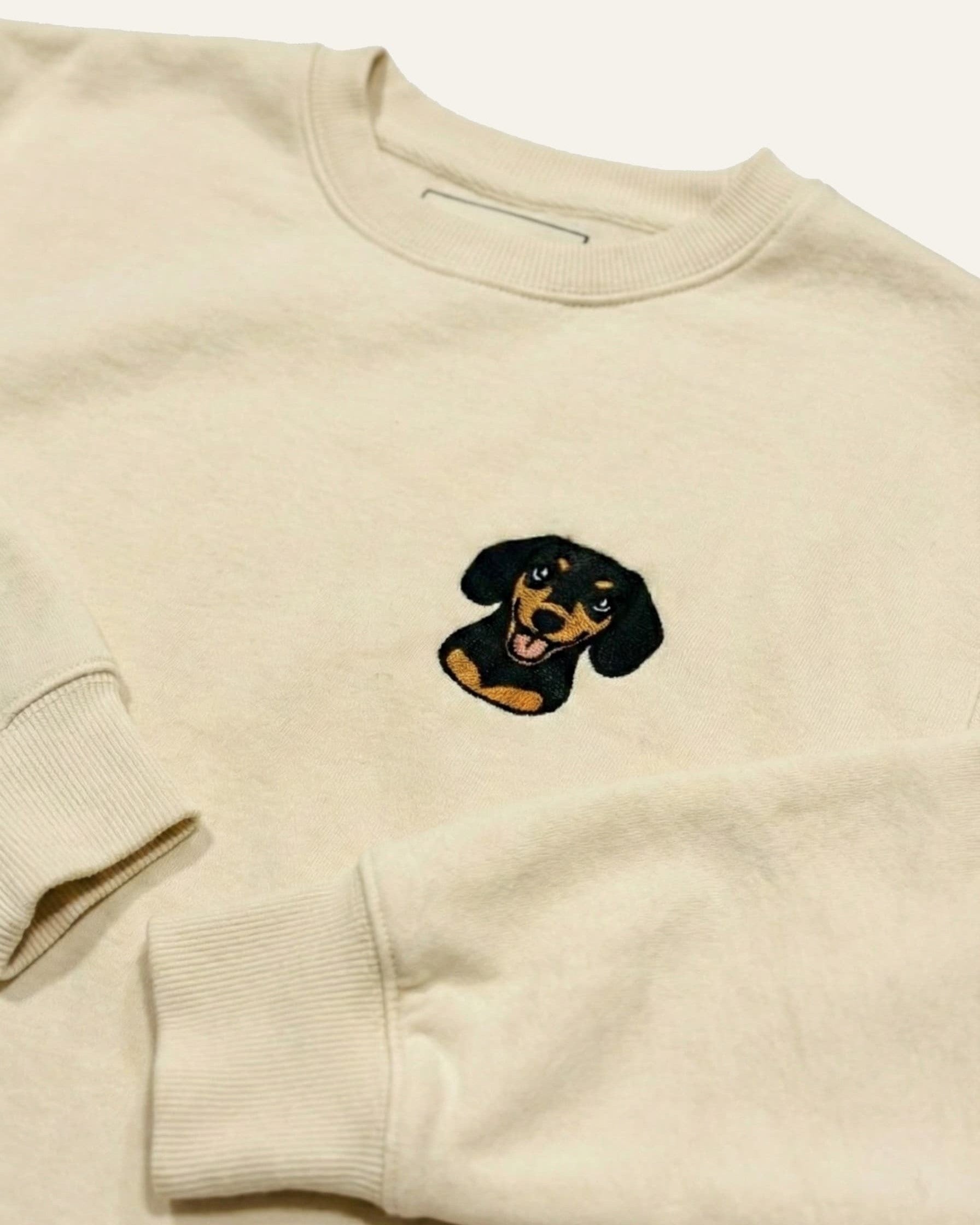 Light Beige Sweatshirt with minimalist embroidered Dachshund icon on left chest.