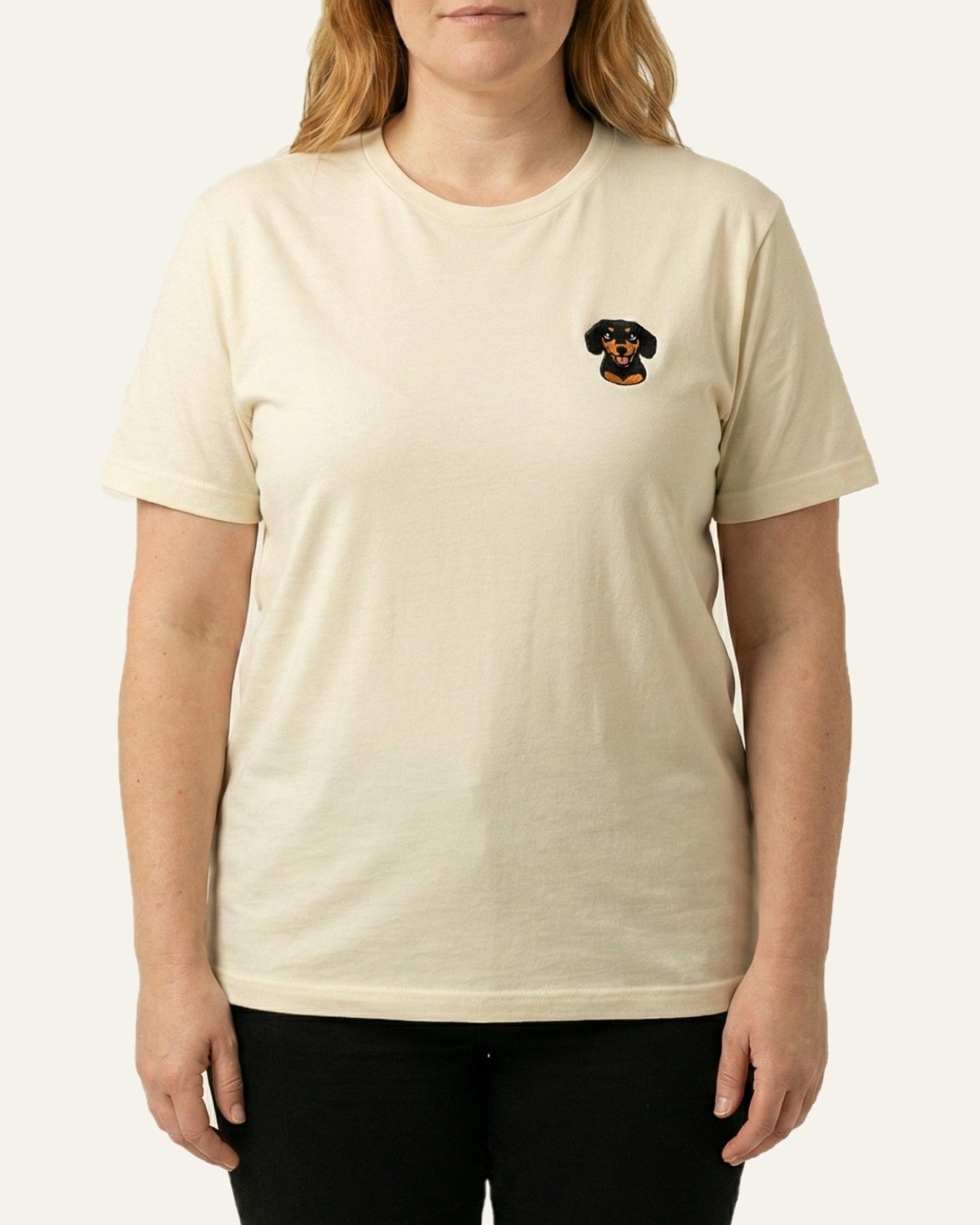 Woman wearing Light Beige T-shirt with minimalist embroidered Dachshund icon on left chest.