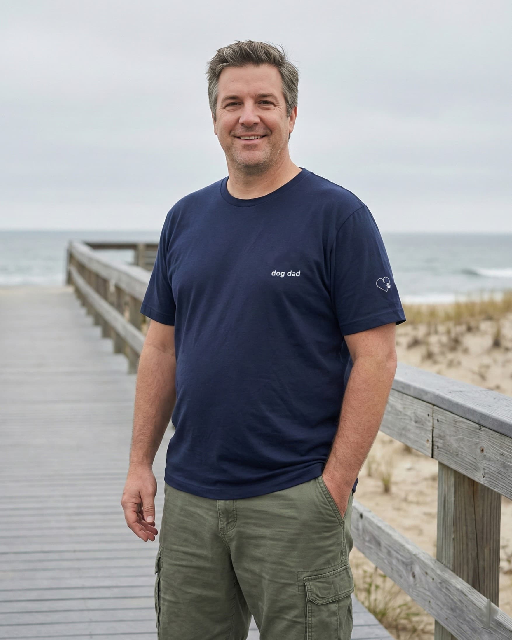 Man wearing Navy t-shirt with minimalist embroidered phrase "dog dad" on left chest. Embroidered Heart and Paw icon on the left sleeve above cuff.
