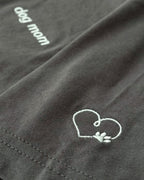 Close up of Asphalt t-shirt with minimalist embroidered phrase "dog mom" on left chest. Embroidered Heart and Paw icon on the left sleeve above cuff.