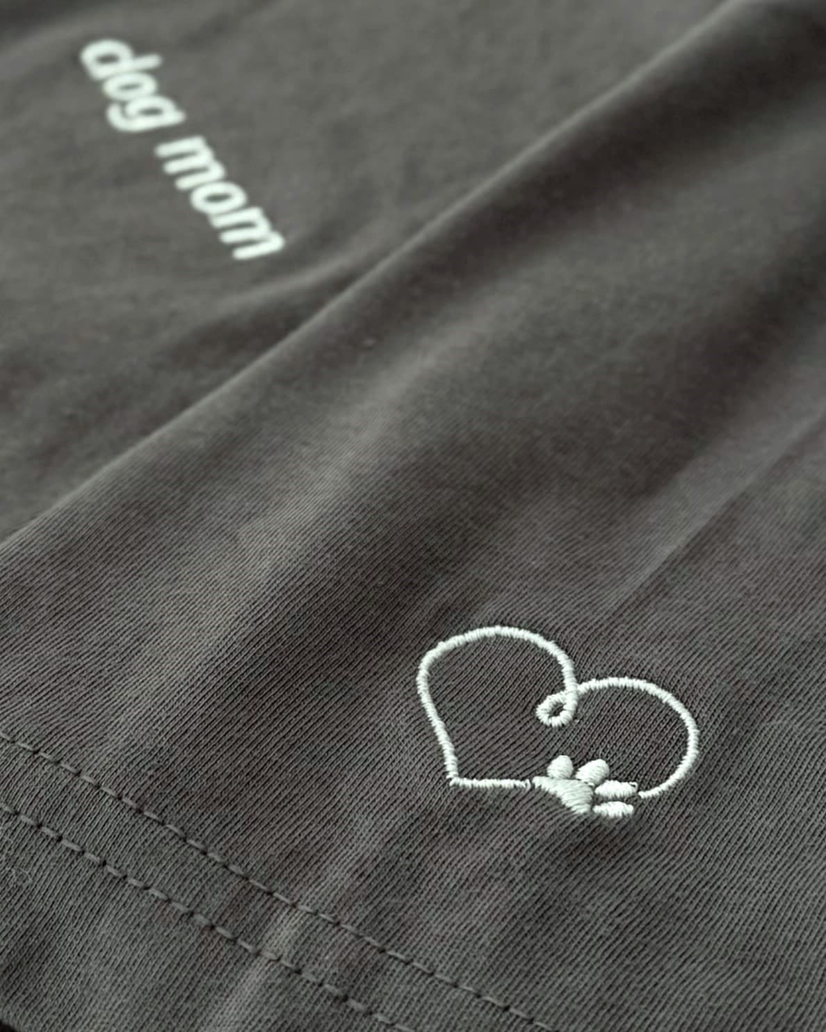 Close up of Asphalt t-shirt with minimalist embroidered phrase "dog mom" on left chest. Embroidered Heart and Paw icon on the left sleeve above cuff.