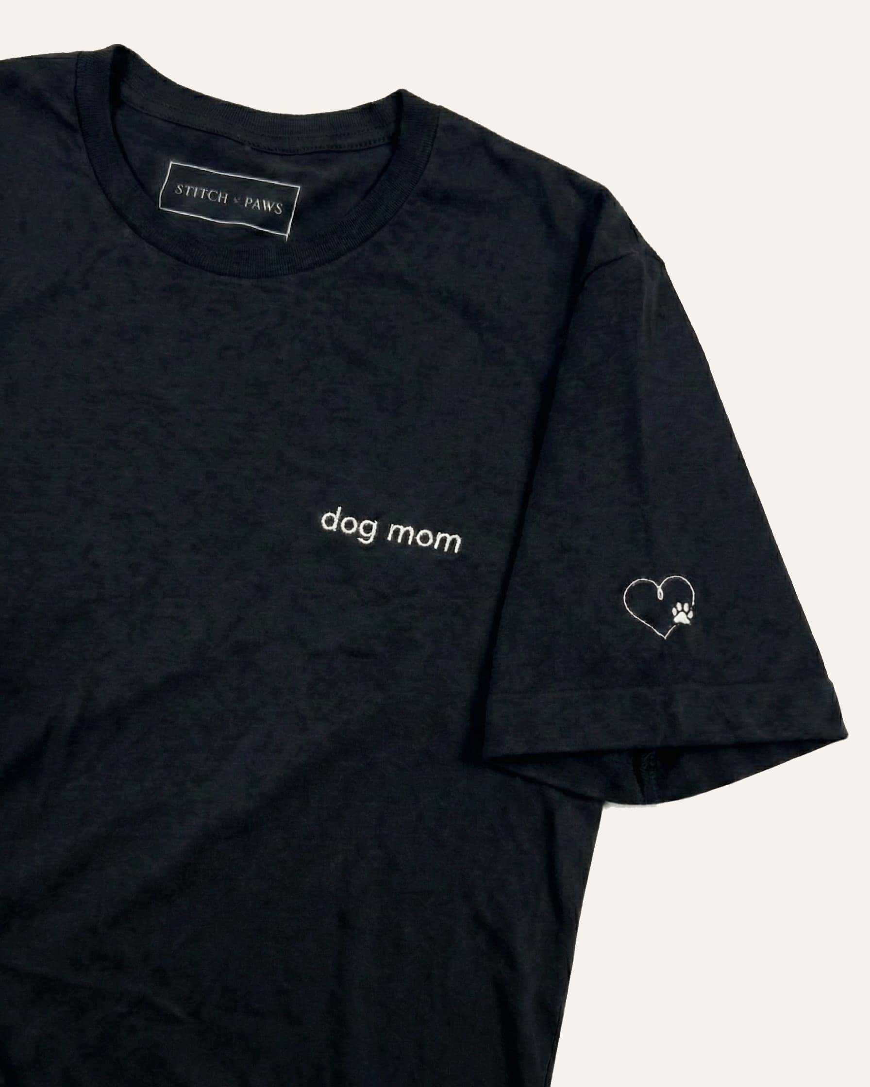 Black t-shirt with minimalist embroidered phrase "dog mom" on left chest. Embroidered Heart and Paw icon on the left sleeve above cuff.