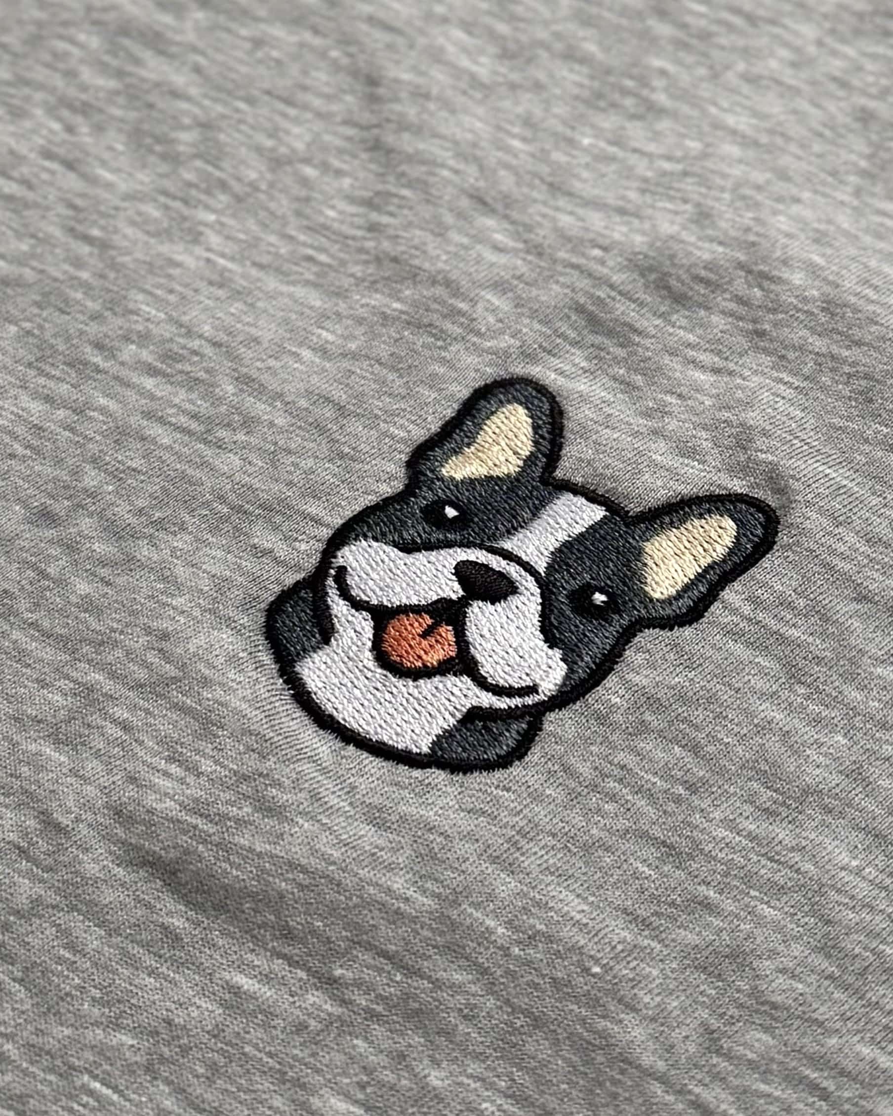 Close-up detail of #blue-pied Frenchie embroidery on Light Grey Heather fabric showing stitch texture.