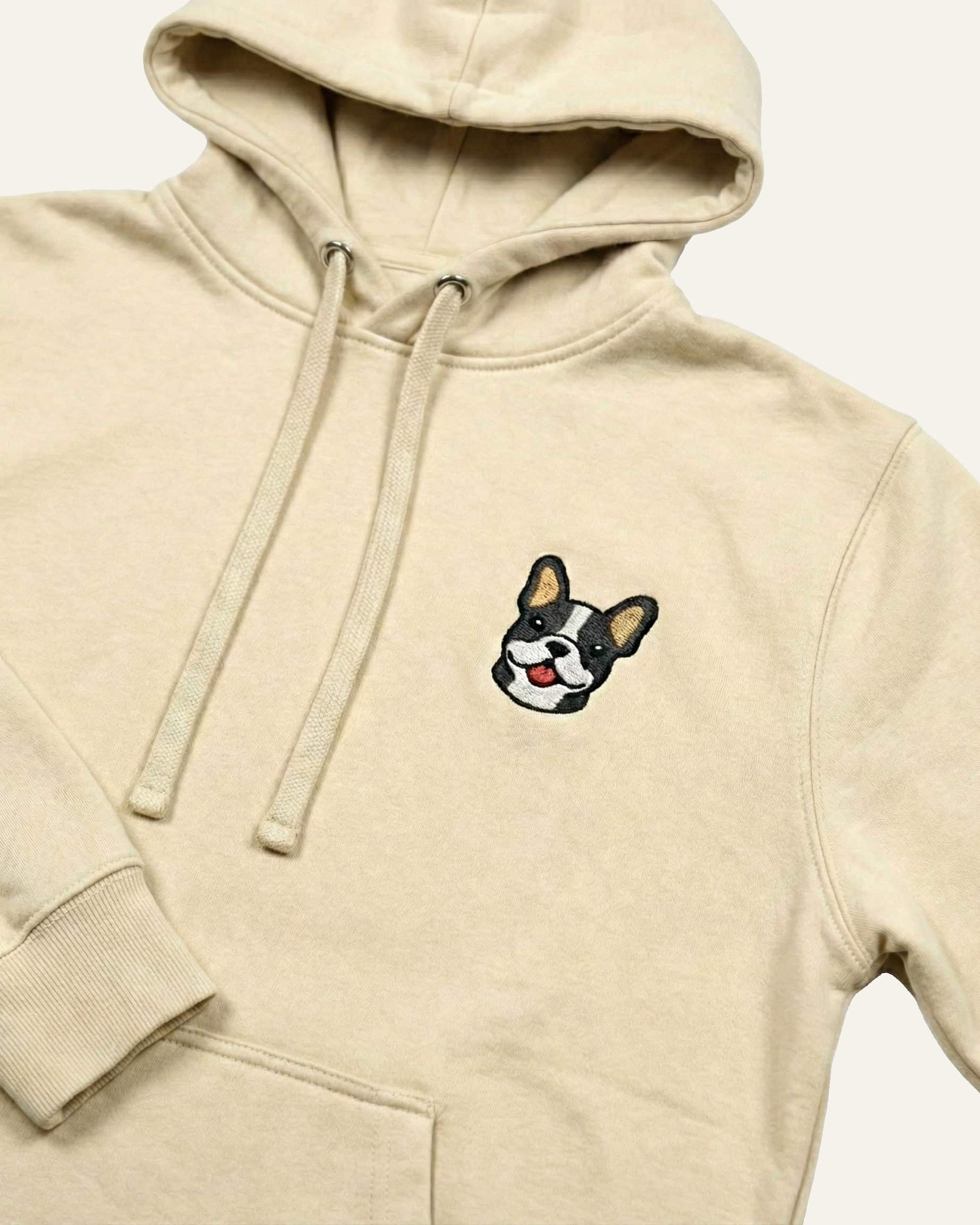 Close up of Beige Hoodie with minimalist embroidered #blue-pied Frenchie icon on left chest.