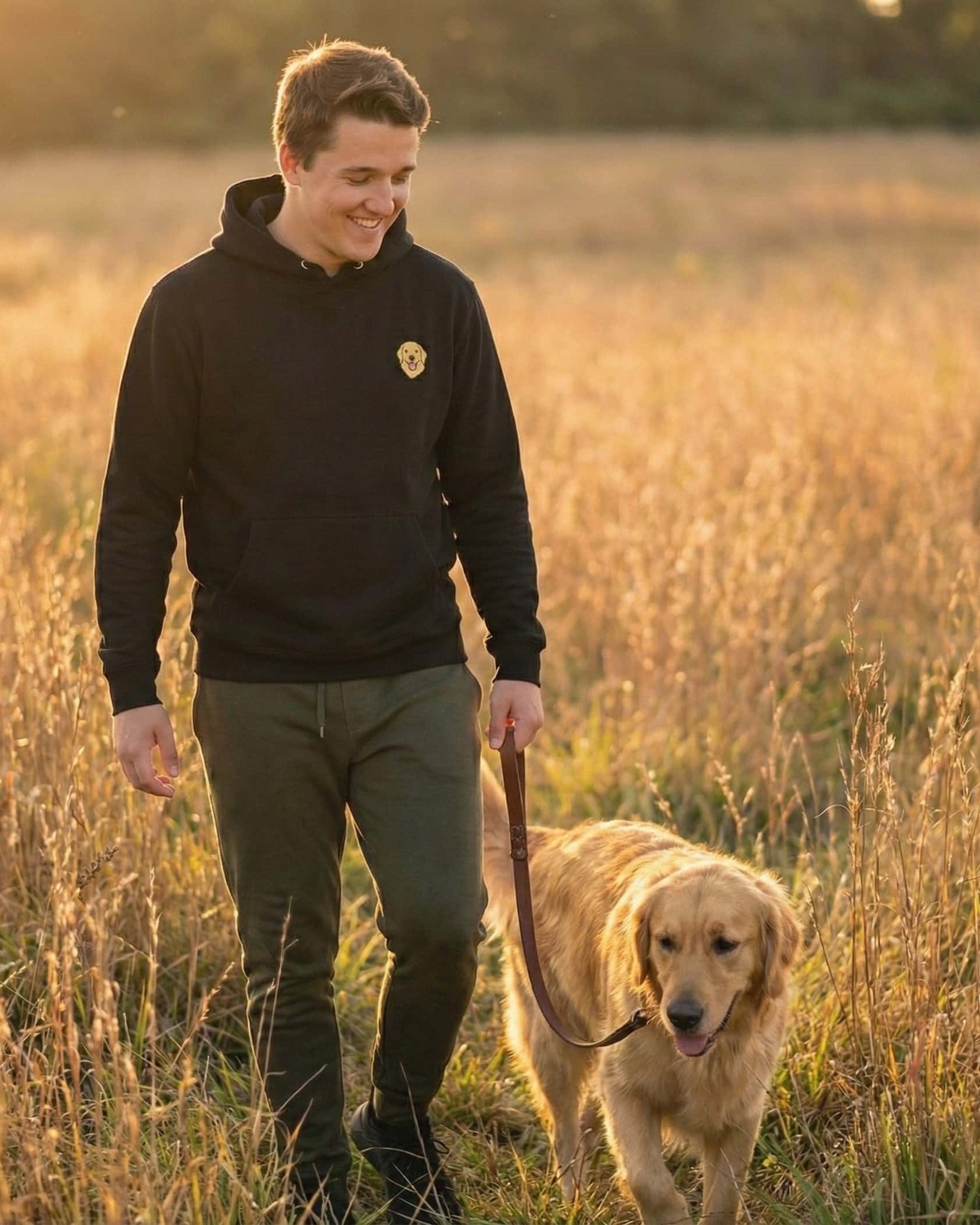 Man walking Golden Retriever in a field, wearing Black Hoodie with minimalist embroidered Golden Retriever icon on left chest.