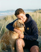 Man hugging Golden Retriever, wearing Navy Hoodie with minimalist embroidered Golden Retriever icon on left chest.