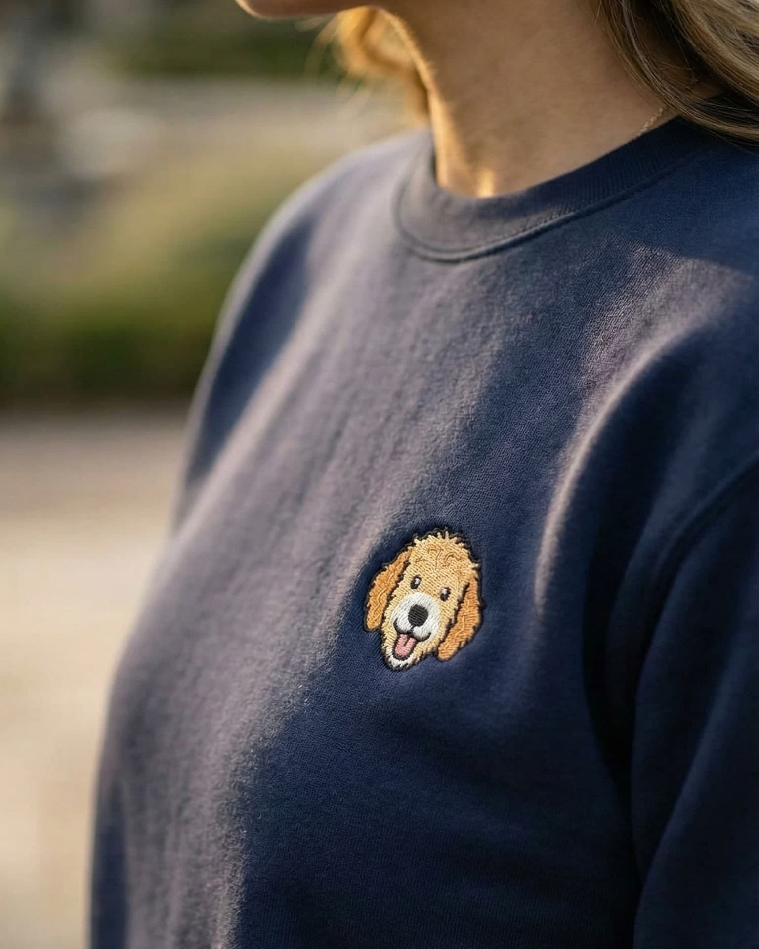 Woman wearing a Navy Sweatshirt with minimalist embroidered Goldendoodle icon on left chest.