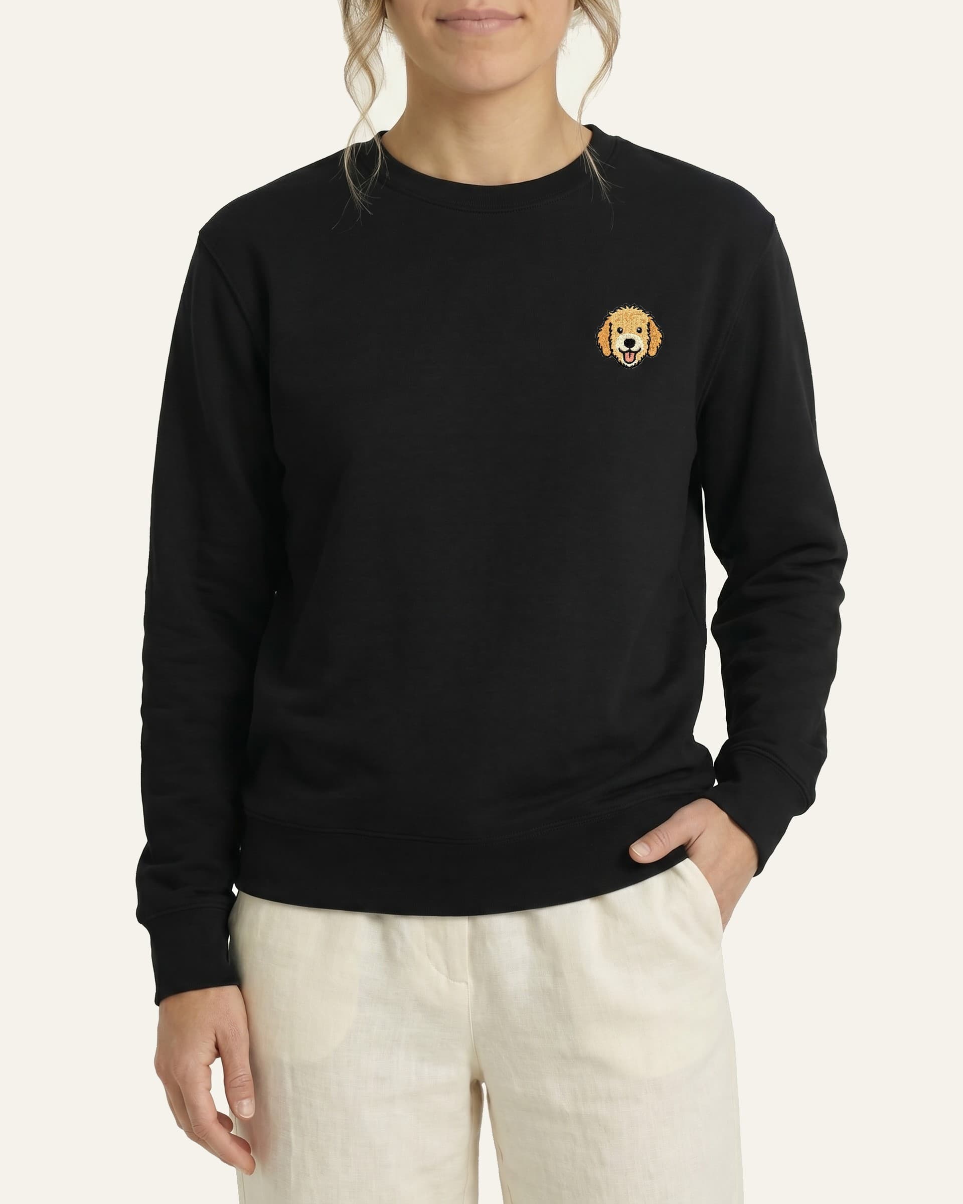 Woman wearing Black Sweatshirt with minimalist embroidered Goldendoodle icon on left chest.