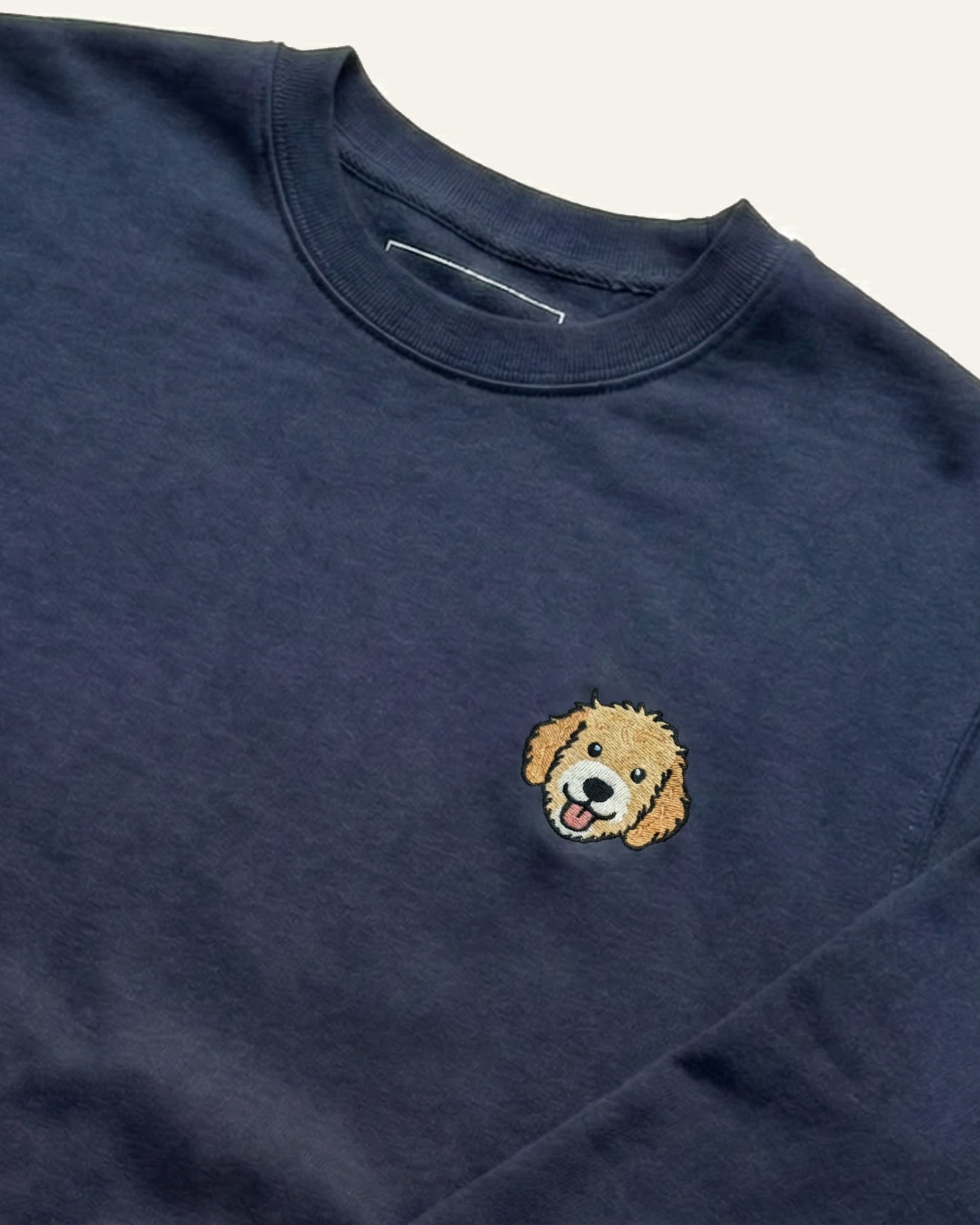 Close up of Navy Sweatshirt with minimalist embroidered Goldendoodle icon on left chest.