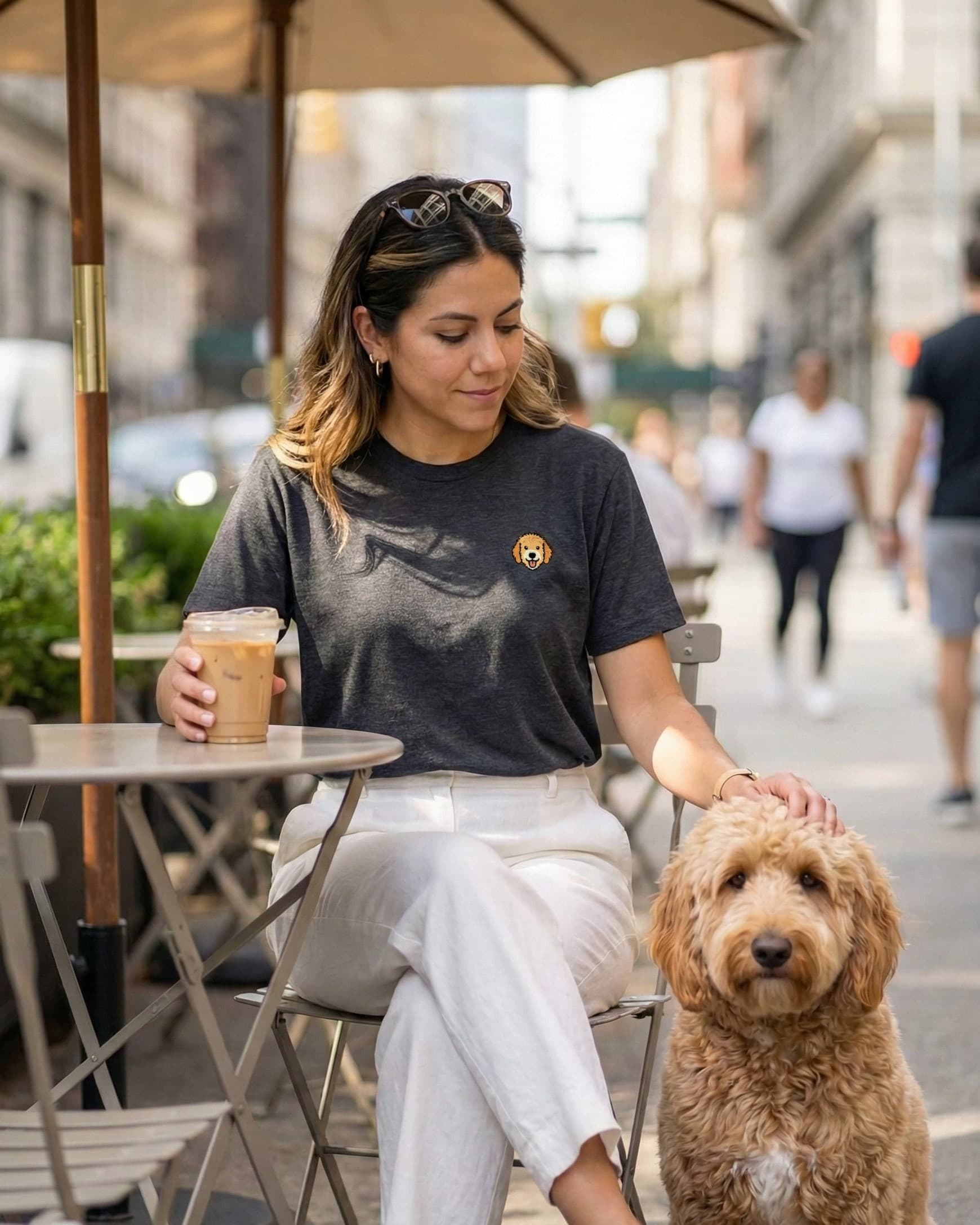 Woman sitting outdoors with a Goldendoodle, wearing Dark Grey Heather T-shirt with minimalist embroidered Goldendoodle icon on left chest.