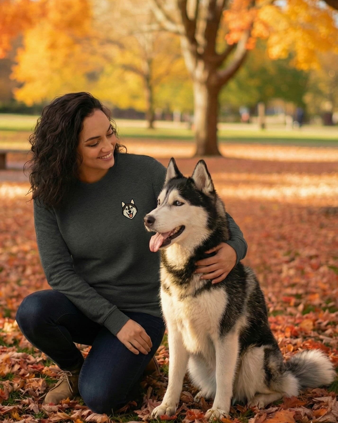 Woman kneeling beside Husky, wearing Dark Grey Heather Sweatshirt with minimalist embroidered Husky icon on left chest.