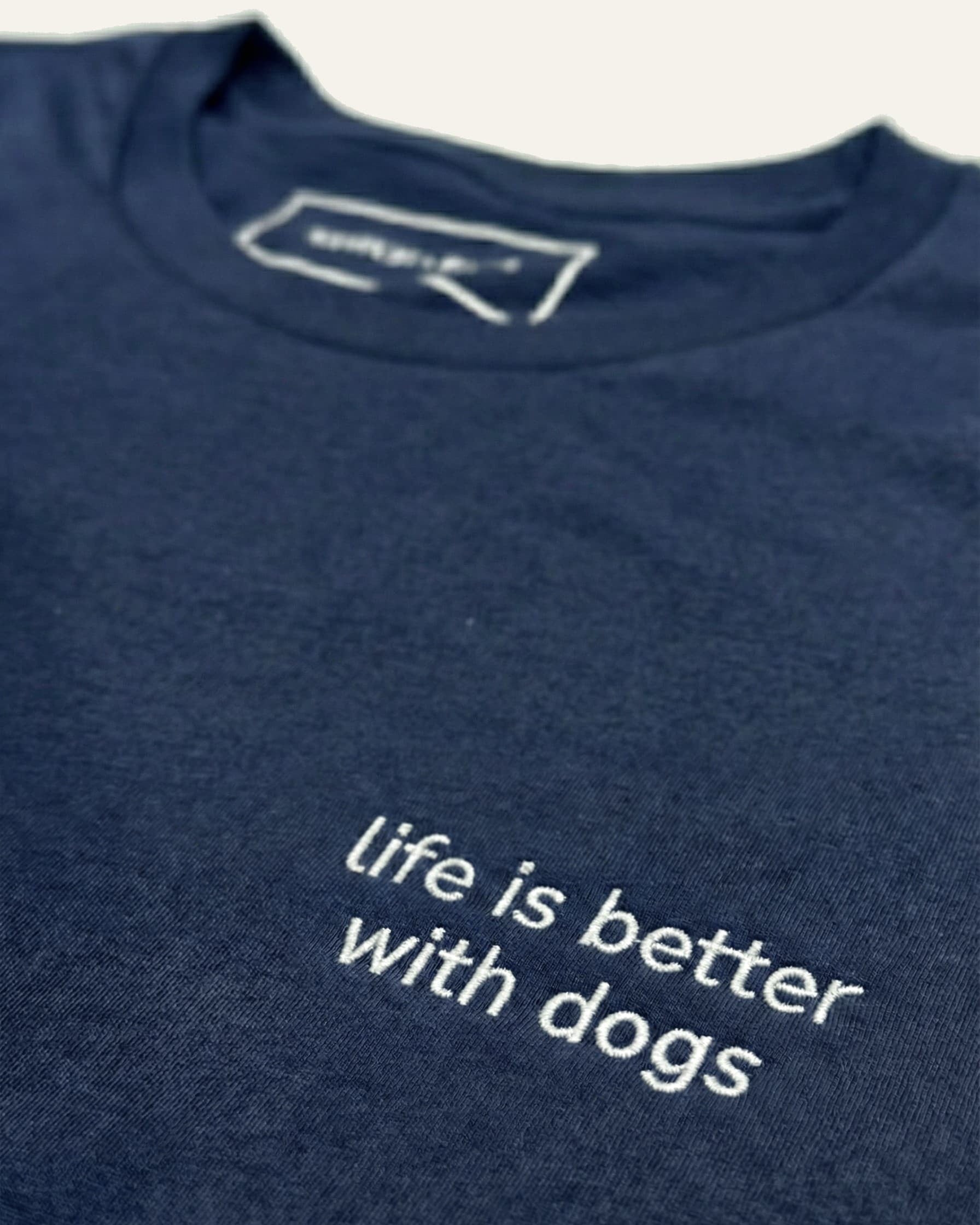 Close up of Navy t-shirt with minimalist embroidered phrase "life is better with dogs" on left chest. 