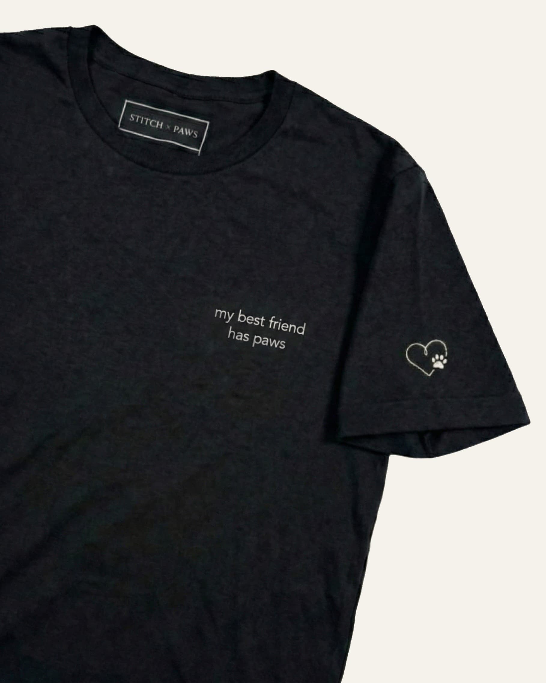 Black t-shirt with minimalist embroidered phrase "my best friend has paws" on left chest. Embroidered Heart and Paw icon on the left sleeve above cuff.