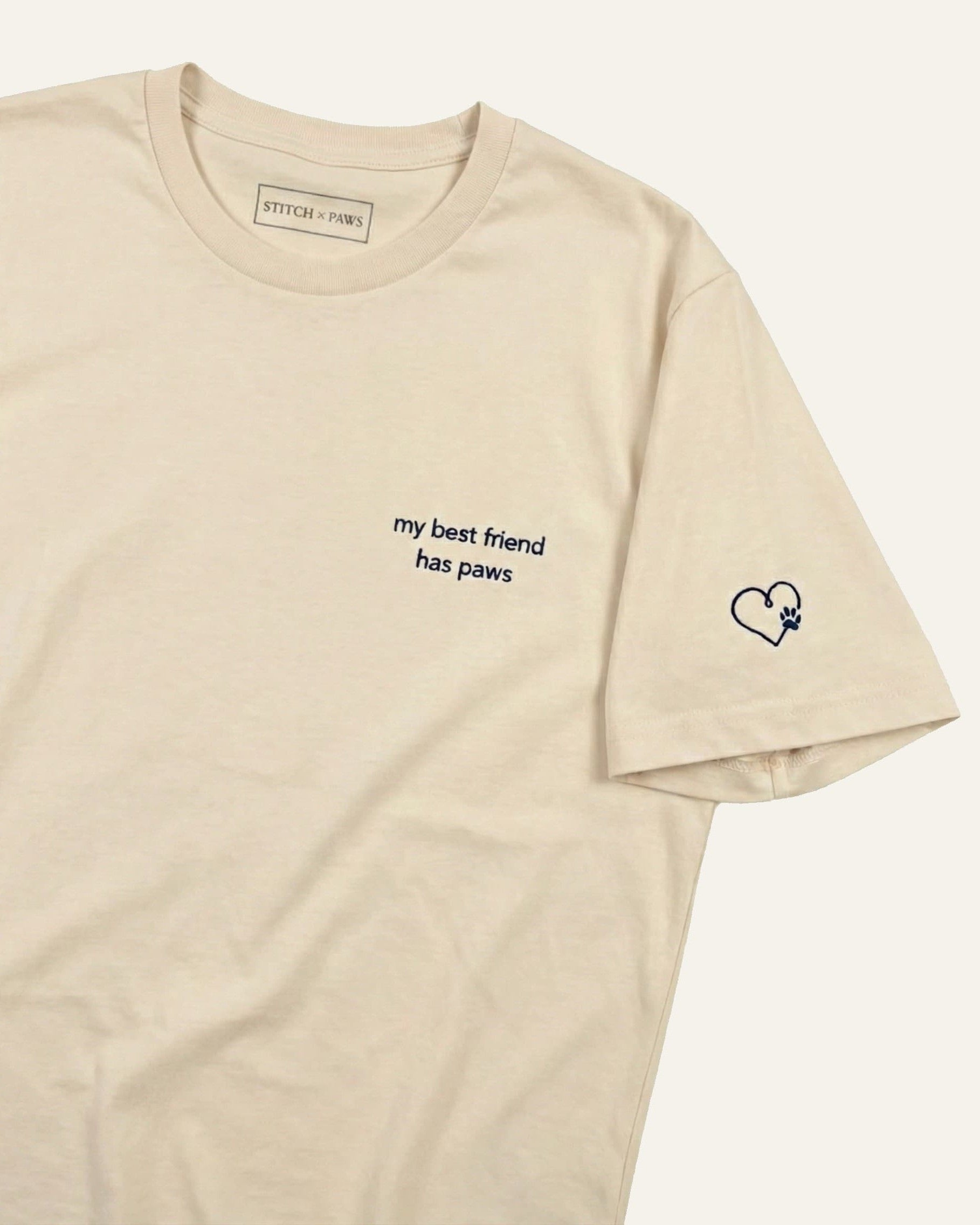 Beige t-shirt with minimalist embroidered phrase "my best friend has paws" on left chest. Embroidered Heart and Paw icon on the left sleeve above cuff.