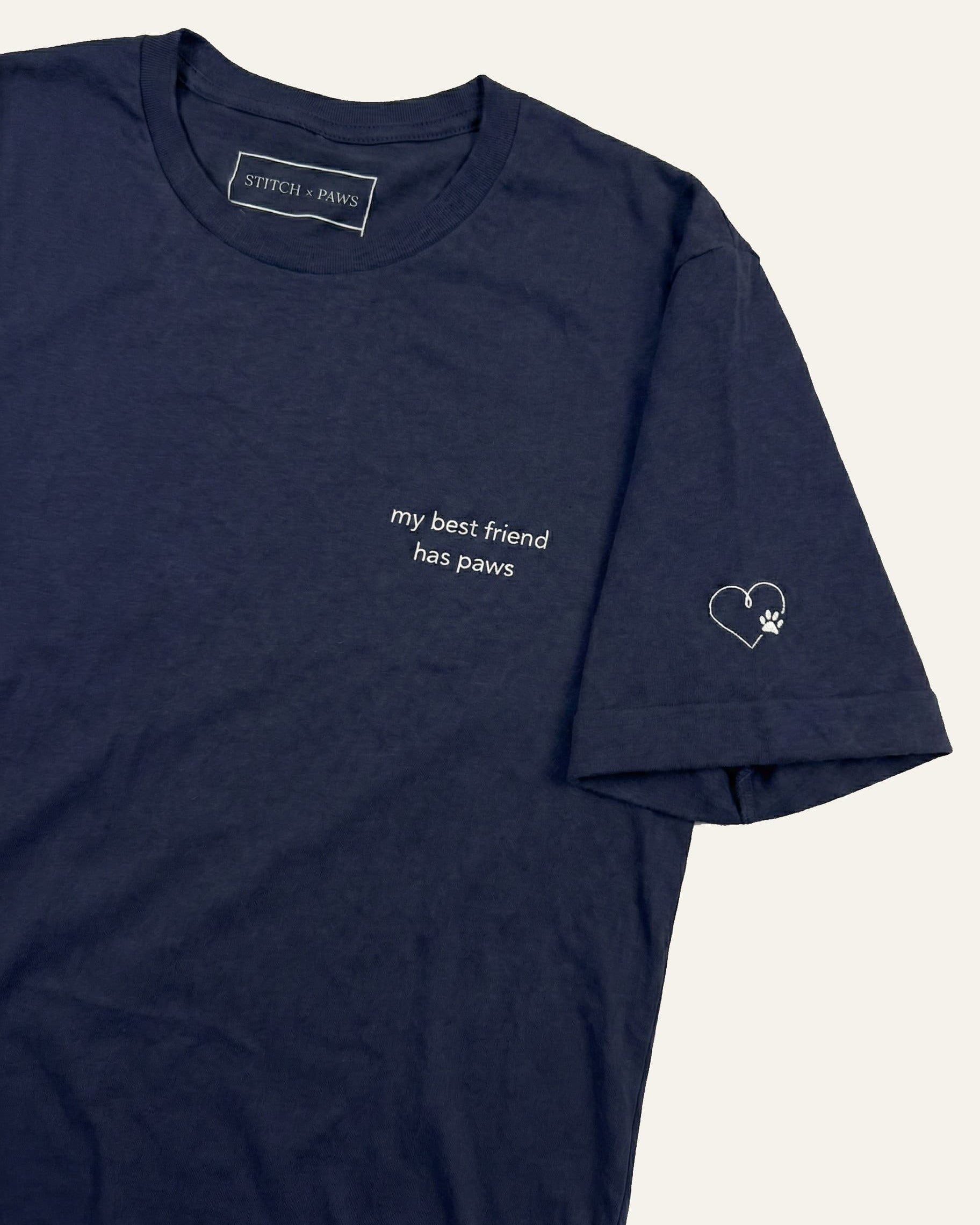 Navy t-shirt with minimalist embroidered phrase "my best friend has paws" on left chest. Embroidered Heart and Paw icon on the left sleeve above cuff.