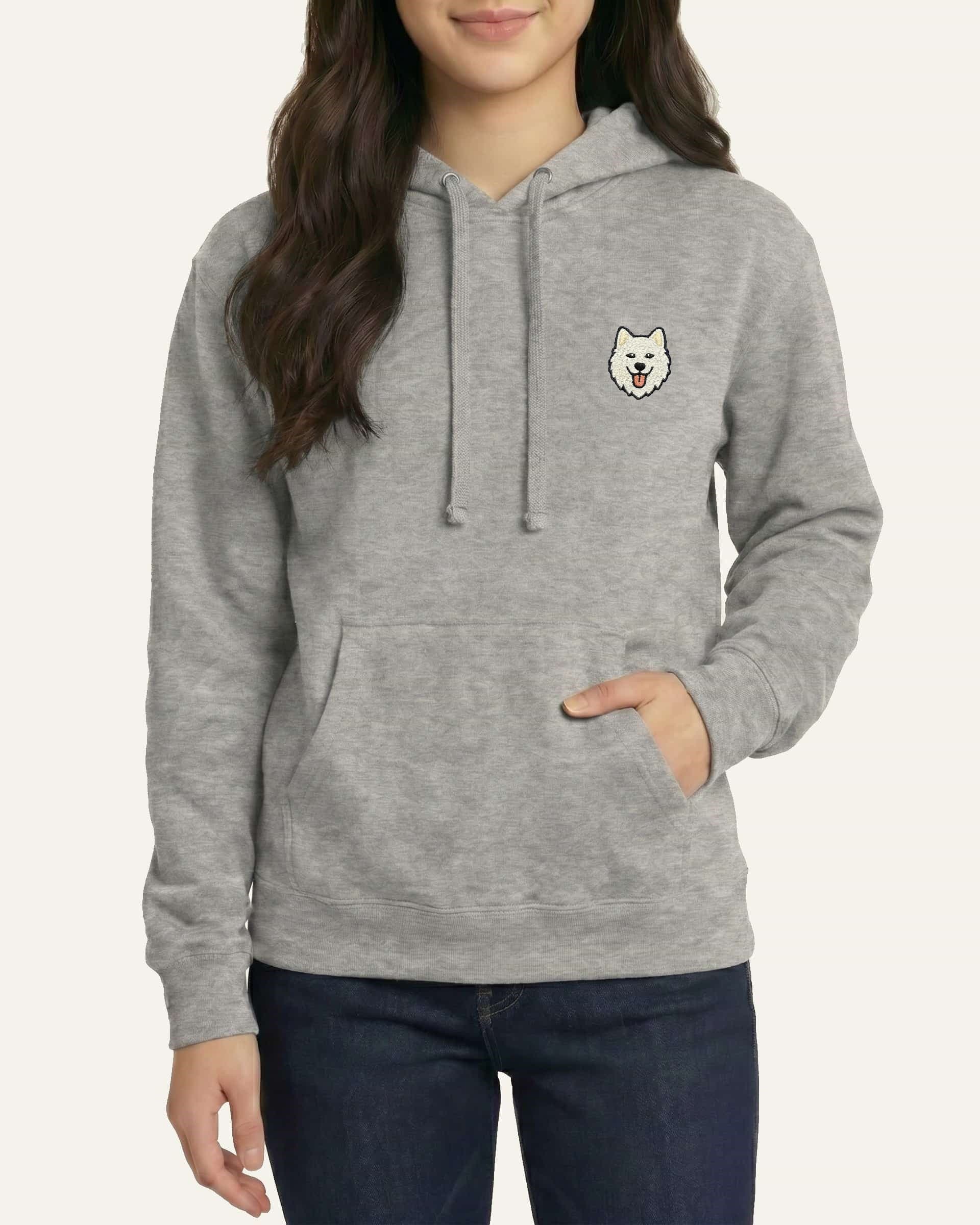 Woman wearing Light Grey Heather Hoodie with minimalist embroidered Samoyed icon on left chest.