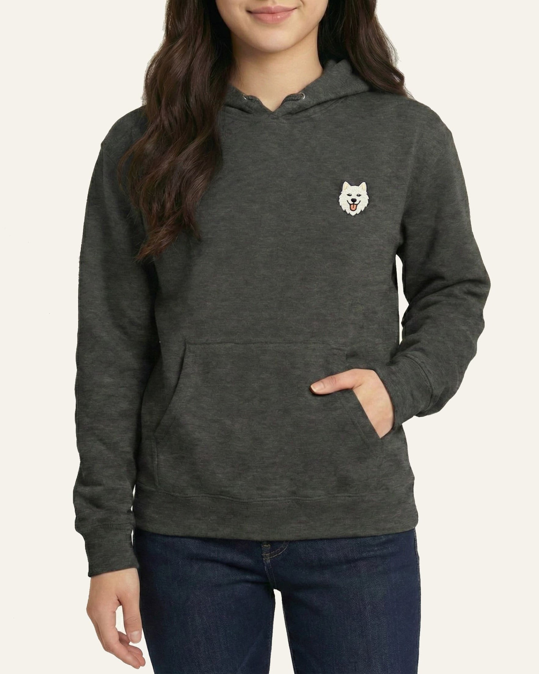 Woman wearing Dark Grey Heather Hoodie with minimalist embroidered Samoyed icon on left chest.