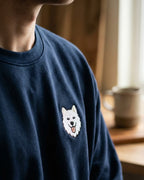 Man wearing Navy Sweatshirt with minimalist embroidered Samoyed icon on left chest.