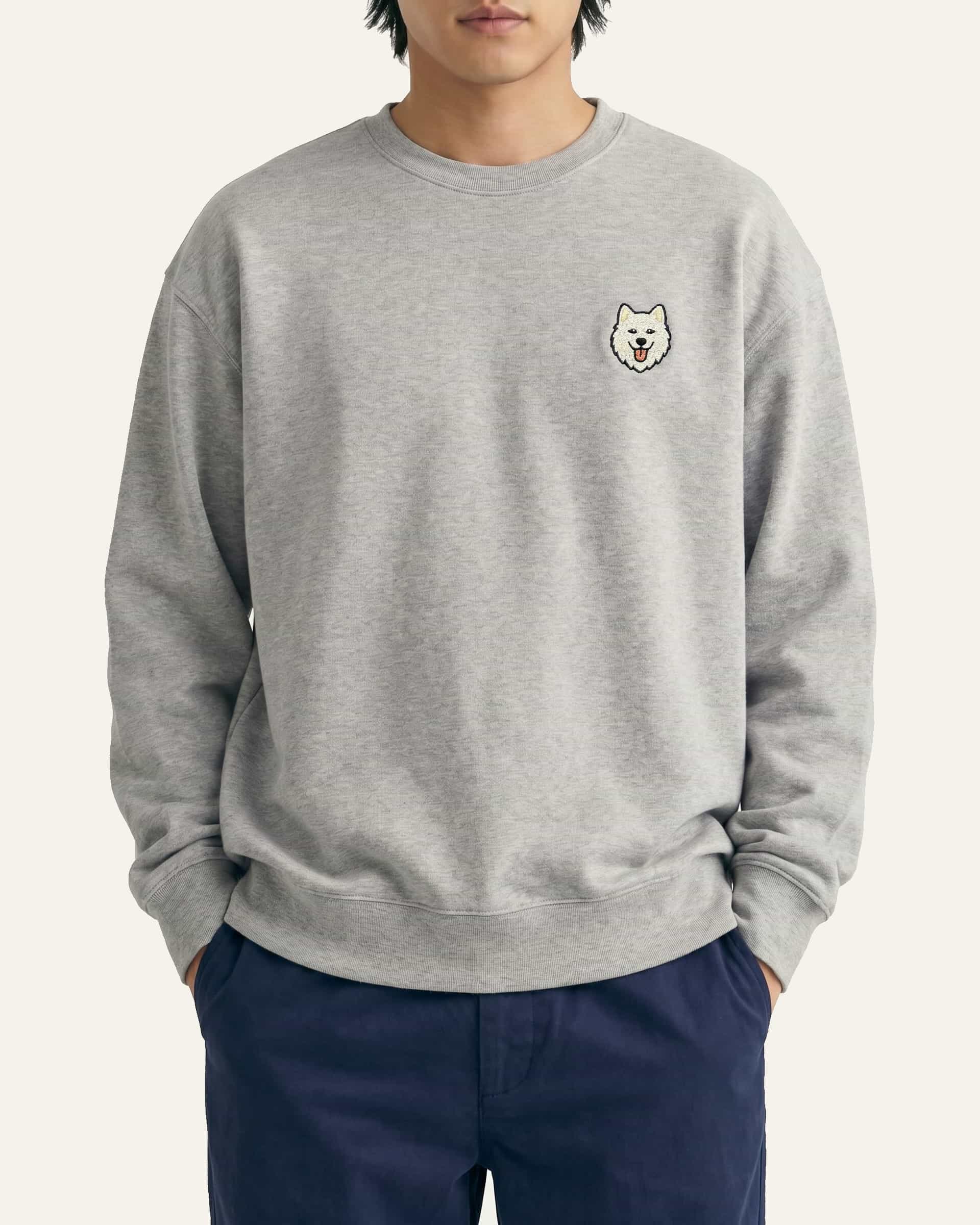 Man wearing Light Grey Heather Sweatshirt with minimalist embroidered Samoyed icon on left chest.