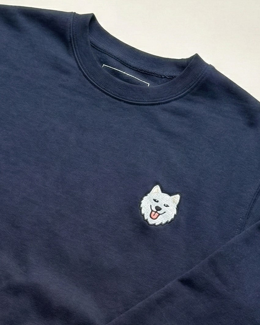 Close up of Navy Sweatshirt with minimalist embroidered Samoyed icon on left chest.