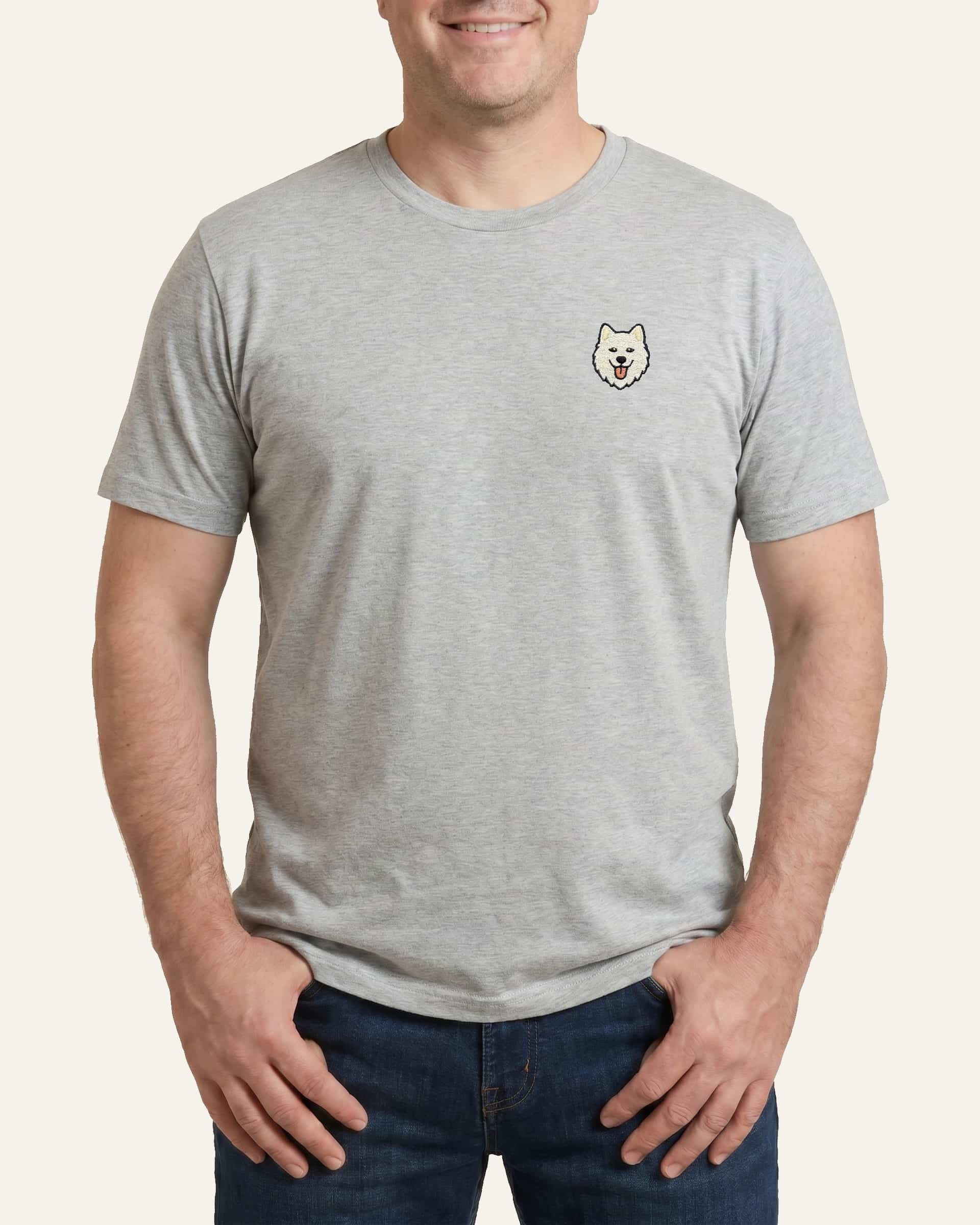Man wearing Light Grey Heather T-shirt with minimalist embroidered Samoyed icon on left chest.