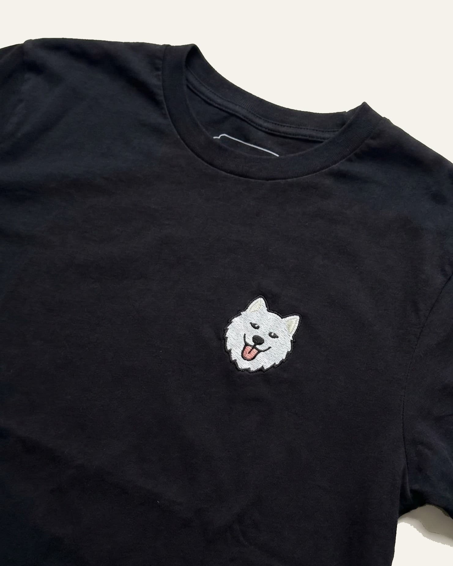 Close up of Black T-shirt with minimalist embroidered Samoyed icon on left chest.