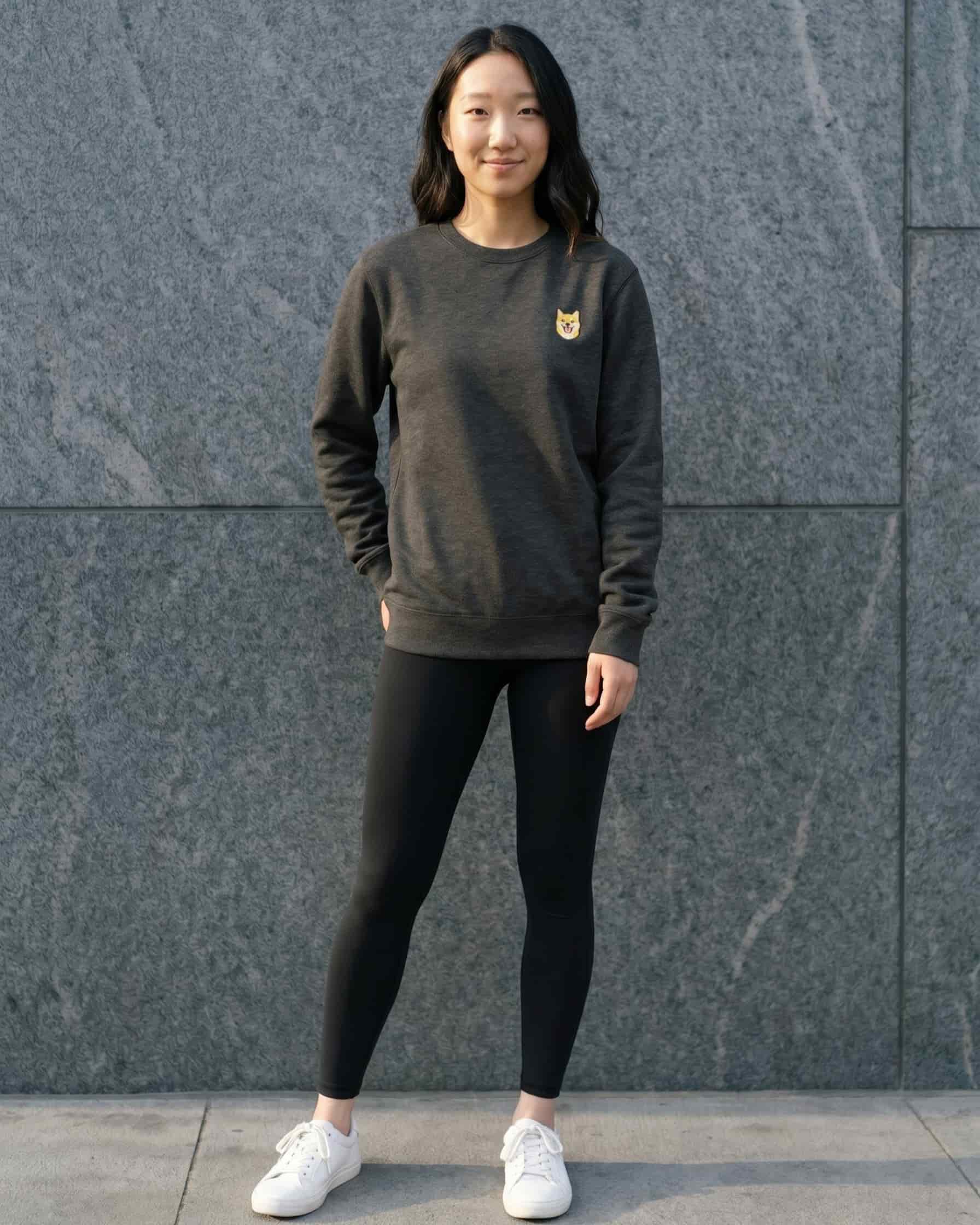 Woman wearing Dark Grey Heather Sweatshirt with minimalist embroidered Shiba Inu icon on left chest.