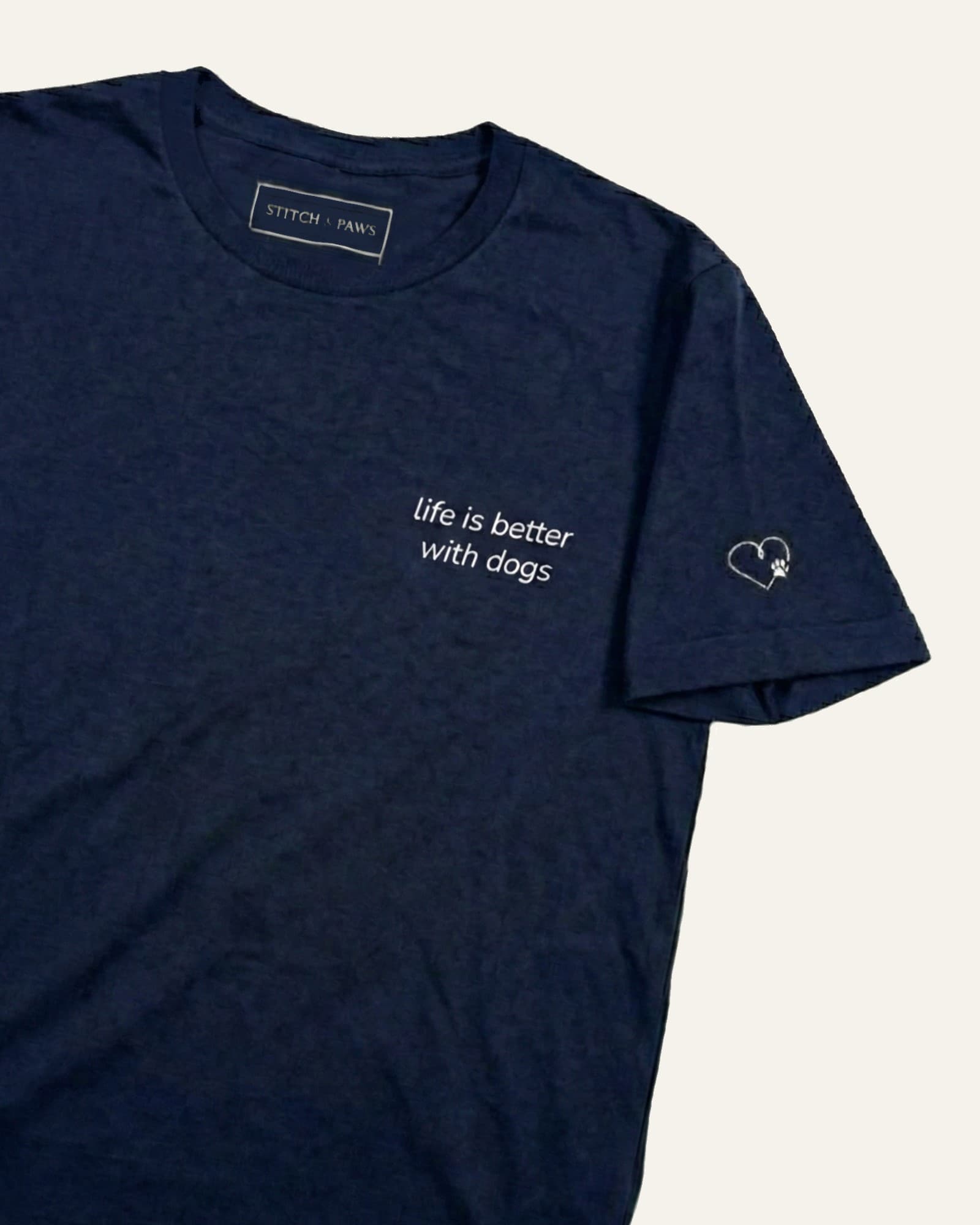 Navy t-shirt with minimalist embroidered phrase "life is better with dogs" on left chest. Embroidered Heart and Paw icon on the left sleeve above cuff.